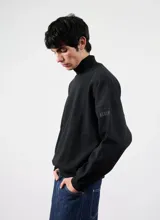 Buzo negro de cuello alto con detalle de la palabra "BESTIA" bordada en el puño.