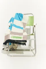 Pareo rectangular de algodón con diseño de damero en tonos celeste, blanco y marrón. Tiene flecos negros en los bordes y la inscripción "SYMPHORINE" en verde.