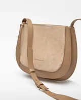Bolso bandolera mediano de piel bovina, color beige y marrón claro, con forma de media luna. Presenta un diseño de doble fuelle con un compartimento frontal en serraje (gamuza) de tono más claro y bordes en piel lisa de tono más oscuro. Tiene asa larga regulable y cierre de cremallera.