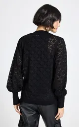 Sweater negro de punto con diseño de doble capa, que combina una base de cuello alto sin mangas con un sobre-sweater de escote en V y mangas largas con calados geométricos.