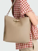 Bolso de hombro tipo bucket en cuero color beige, con cierre de pasador metálico característico de la línea Le Roseau y correa ajustable.