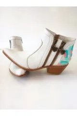 Bota corta de cuero blanco estilo tejano, con diseño pintado a mano en tonos celeste y rosado en el talón. Posee doble cierre lateral con tiradores metálicos triangulares, taco cuadrado de madera y punta fina.