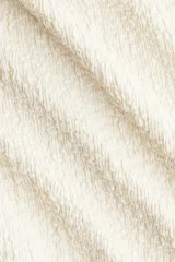 Vestido midi color crema con textura arrugada, de corte ajustado. Presenta un diseño asimétrico de un solo hombro, con tirante fino adornado con anillas metálicas doradas en un lado, y un corte ancho en el otro. Tiene frunces laterales que generan un efecto drapeado.