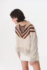 Buzo de tejido de punto en color azul marino, con cuello alto y cierre frontal parcial. Presenta un diseño con franjas en color marrón y detalles de líneas en rojo en el pecho, hombros y ruedo. Tiene corte holgado y mangas largas con puños acanalados.