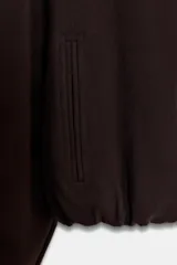 Chaqueta de corte corto y diseño abullonado en color marrón oscuro, con cuello solapa, mangas largas con puños elásticos y cierre frontal con cremallera metálica. Cuenta con bolsillos delanteros de doble vivo.