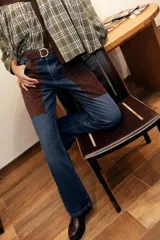 Jean de corte recto y tiro medio, confeccionado en denim celeste con inserciones de cuero marrón en las piernas que simulan chaparreras.