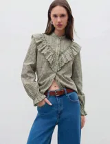 Camisa de manga larga con estampado de cuadros vichy en tonos verde oliva y crudo. Presenta cuello mao, cierre frontal con botones y volados decorativos en la parte delantera. Las mangas terminan en puños elastizados con un ligero acabado de volado.
