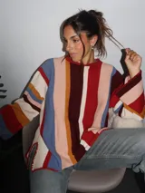Sweater tejido a mano con terminaciones en crochet, de silueta oversize y mangas acampanadas. Presenta un diseño de rayas verticales multicolores en tonos tierra, rojo, azul y crema.