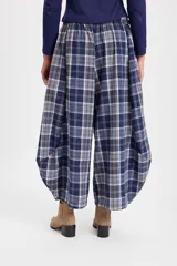 Pantalón de corte holgado con silueta tipo balloon, confeccionado en tela a cuadros. Presenta cintura elástica con cordón ajustable y cortes laterales circulares que aportan volumen a la prenda.