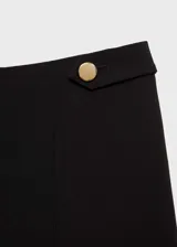 Pantalon de vestir negro de corte recto y diseño crop, confeccionado en tejido fluido con tiro medio. Presenta cierre frontal con botón, gancho y cremallera, además de detalles de botones decorativos en la cintura.
