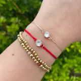Pulsera de hilo con dije circular de circnia con baño en oro y cierre regulable.