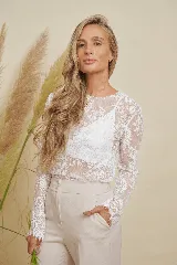 Blusa de encaje blanco translúcido, con escote redondo y mangas largas.