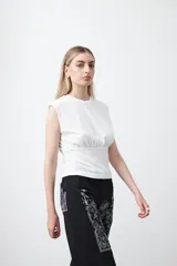 Top sin mangas de tejido acanalado color blanco, con cuello redondo, hombros definidos y detalle de frunce bajo el busto que aporta estructura.