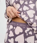 Conjunto de pijama compuesto por una blusa de manga larga con cuello redondo y un pantalón con cintura elástica. Ambas piezas presentan un diseño estampado de corazones en tonos lila y crema.
