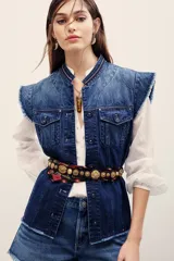 Chaleco de denim azul de corte estructurado y sin mangas, con cuello mao y cierre frontal con botones. Presenta bolsillos frontales con solapa y detalles deshilachados en las sisas y el ruedo.