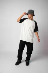 Remera estilo raglán color blanco en el cuerpo, con mangas en tono tostado y ribetes en color verde militar en el cuello y los puños.