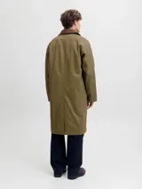 Campera larga de corte clásico, color verde oliva, con cuello de pana en contraste color marrón y cierre frontal de botones. Presenta un diseño funcional con bolsillos laterales integrados y estructura resistente.