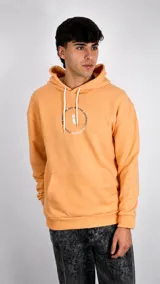 Hoodie color naranja con capucha y cordones ajustables en color blanco. Presenta un estampado circular en el pecho con el logo de la marca y la frase 'Focus on finding joy in the journey'. Incluye bolsillo frontal tipo canguro.