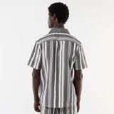 Camisa de manga corta con cuello solapa y cierre frontal de botones, con diseño de rayas verticales en tonos negro y blanco.