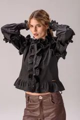 Camisa celeste con volados decorativos en los hombros, pecho, mangas y ruedo, destacados con ribetes en tono rojo. Presenta cierre frontal de botones, cuello alto y mangas largas abullonadas con puños ajustados.