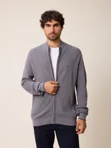 Cardigan de punto gris con cierre frontal completo, cuello tipo mao y puños acanalados. Presenta un pequeño logo bordado en el pecho y detalles en contraste en el interior del cuello y puños.