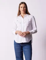 Camisa blanca de algodón con cuello clásico, escote en V y cierre frontal con botones. Presenta apliques de brillos plateados en el frente y mangas largas con puños abotonados.