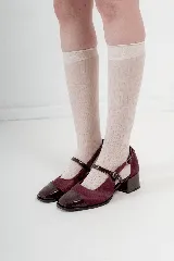 Zapatos tipo Mary Jane de cuero color bordó y charol, con punta cuadrada y taco bajo. Tienen una tira con hebilla sobre el empeine y recortes laterales.