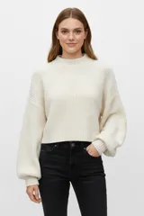 Sweater de tejido de punto grueso color blanco roto, con cuello redondo y mangas largas abullonadas. El calce es holgado y corto (cropped).