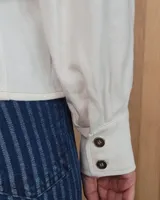 Camisa de color arena con mangas abullonadas, puños anchos con botones y cuello clásico. Presenta un diseño de corte recto con costuras visibles y cierre frontal oculto.