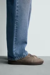 Zapatilla de estilo urbano confeccionada en piel con acabado de serraje en color marrón. Presenta cierre mediante cordones al tono, detalle de pespuntes en el empeine y suela de goma a tono.