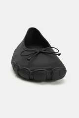 Zapato tipo bailarina deportiva de color negro, con suela de goma y detalle de lazo en la puntera redonda.