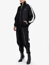 Chaqueta de estilo deportivo y corte oversize, color negro con franjas blancas en las mangas y cuello alto. Cuenta con cierre frontal completo de cremallera y bolsillos laterales.