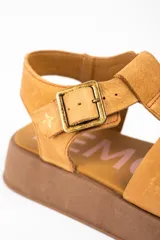 Sandalia tipo guillermina de cuero color camel, con diseño de tiras anchas entrelazadas, cierre con hebilla metálica lateral y suela de plataforma plana en tono marrón.