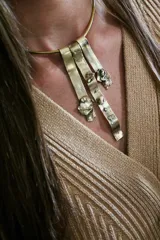 Gargantilla rígida de bronce con tres tiras colgantes irregulares y detalles rústicos.