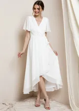 Vestido blanco de gasa con escote en V, corte imperio, mangas cortas tipo mariposa y falda asimétrica con ruedo más corto en el frente y más largo en la espalda.