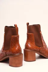 Bota tipo botineta de cuero negro con diseño trenzado artesanal en toda la capellada. Presenta paneles laterales elásticos, taco cuadrado de altura media y tirador en la parte superior trasera.