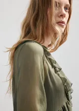 Vestido midi color verde militar, confeccionado en tejido fluido de poliéster. Presenta un diseño evasé, escote de pico con volantes, y mangas largas con puños elásticos. Incluye detalles de volantes en el cuello y forro interior.
