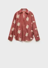 Camisa de manga larga en color terracota con diseño semitransparente. Presenta cuello camisero, cierre frontal con botones y bordados florales en color blanco distribuidos por toda la prenda.
