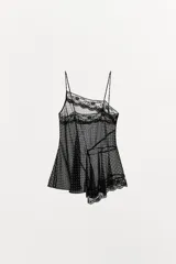 Top de tirantes finos con estampado de lunares, confeccionado en tejido semitransparente. Presenta detalles de encaje en el escote y un bajo asimétrico con volantes.