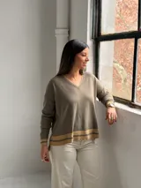Sweater de punto en color verde oliva, con cuello en V y diseño holgado. Presenta detalles de franjas en color beige en el cuello, los puños y el ruedo.