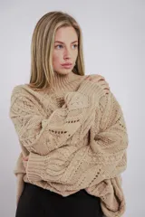 Buzo de tejido de punto grueso en color negro, con cuello alto y diseño de trenzas y relieves en toda la prenda. Presenta mangas largas con terminación ajustada y corte holgado.