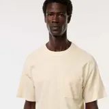 Camiseta de manga corta color crema, con cuello redondo y un bolsillo de parche en el lado izquierdo del pecho.