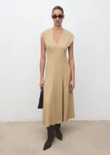 Vestido midi de corte evasé en color beige, con cuello en pico y manga corta. Presenta un diseño con costuras verticales decorativas y cierre de cremallera en la parte posterior.