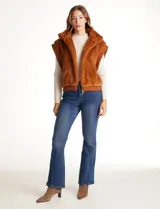 Chaleco de piel sintética en color beige, con cuello alto, cierre frontal metálico y terminaciones en tejido rib en el ruedo y sisas.