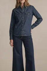 Camisa de jean azul oscuro, de corte ajustado, con cuello clásico, botones frontales, dos bolsillos con solapa en el pecho y mangas largas con puños abotonados.