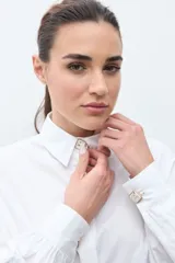 Camisa blanca de corte recto con cuello clásico, cierre frontal de botones y mangas largas con puños abullonados.