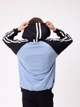 Canguro con capucha de estilo deportivo, con cuerpo en color celeste y mangas raglán en color negro. Presenta el logo de la marca estampado en el pecho, bolsillo tipo canguro frontal y franjas blancas laterales en las mangas.