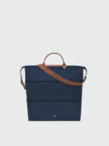 Bolso de viaje Longchamp modelo Le Pliage Original, de diseño ampliable, confeccionado en nylon negro con detalles en cuero marrón en las asas y solapa frontal con cierre de botón a presión. Incluye correa ajustable y extraíble.