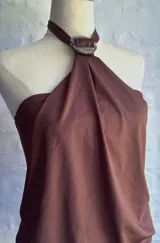 Vestido corto color marrón con diseño de cuello halter, caracterizado por un detalle de argolla circular en el centro del escote y una caída fluida y drapeada en la parte superior, contrastando con una falda ajustada.