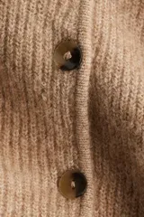 Saco de punto acanalado con cuello redondo, cierre frontal con botones y diseño de peplum con vuelo en la cintura.
